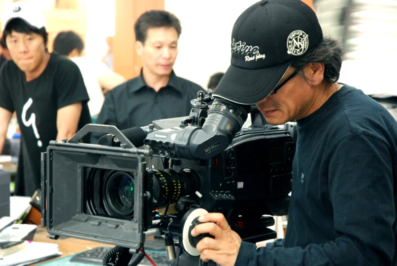 an asian man holding a camera and looking at it
