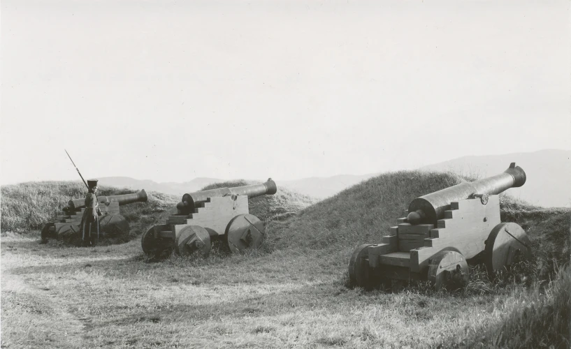 old military equipment sit in the dirt near a hill