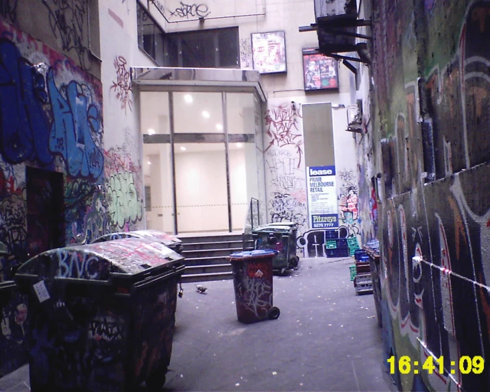 a very large graffiti covered building with some tables and garbagecans in the alley