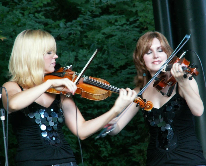 two women with blonde hair playing violin on stage