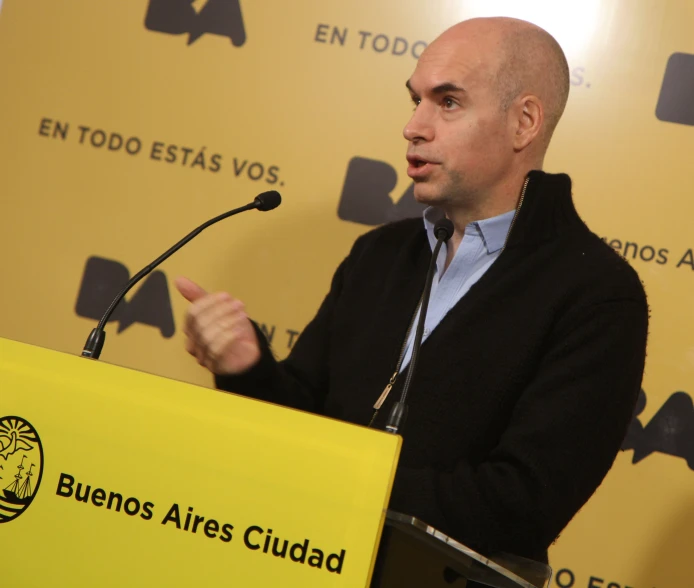 balding man in a black sweater speaking at a podium