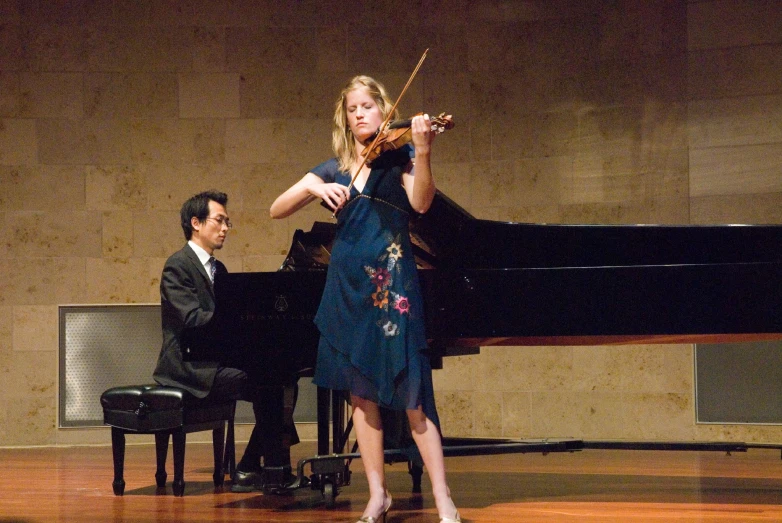 woman in blue dress playing violin with a man in black suit