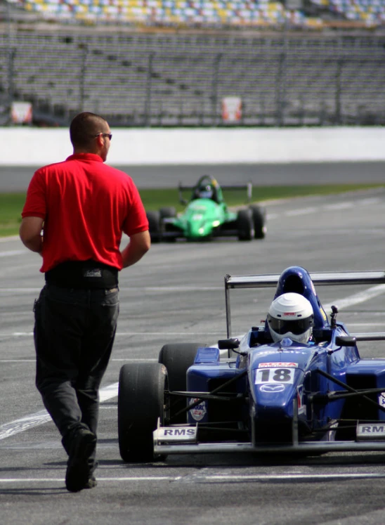 a man walking toward a blue race car on a track