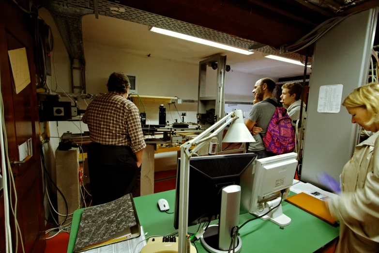 several people in a large industrial office with various computers and electronics