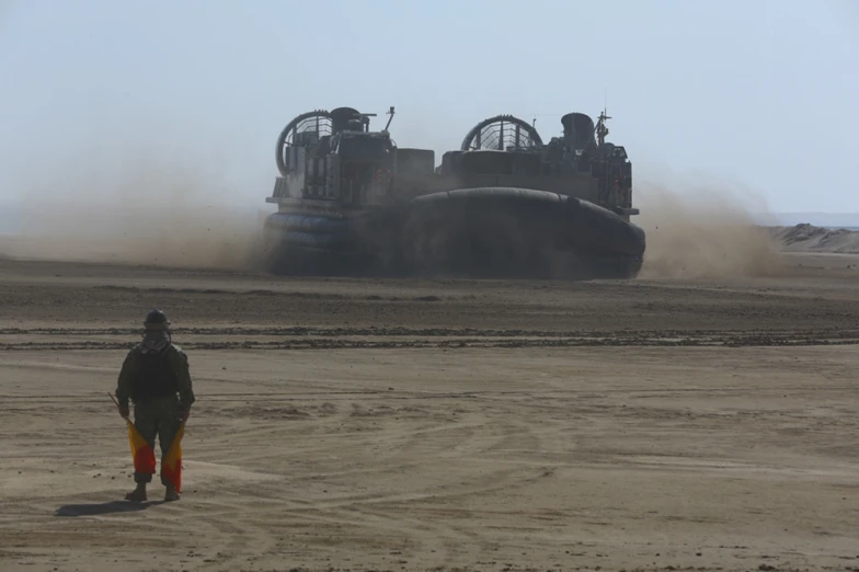 a man stands in the middle of a dirt field near an industrial machine