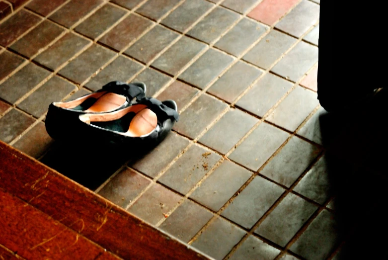 a black shoe and white shoes sitting on tiled floor