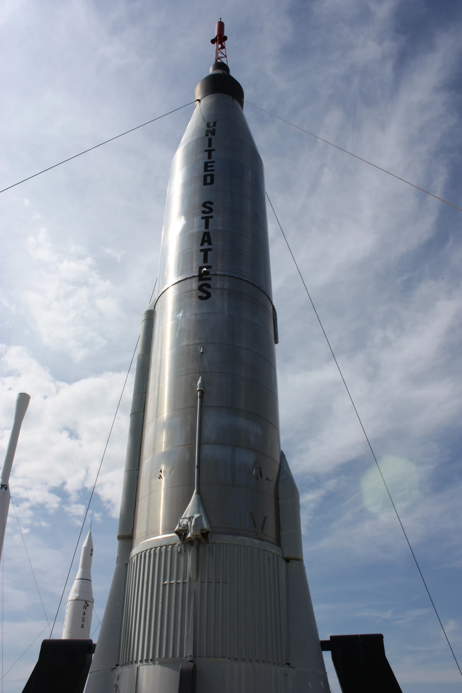 a tall stainless steel rocket against a cloudy blue sky