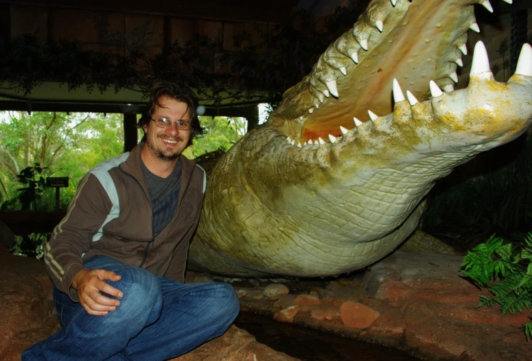 a man sitting next to a fake alligator on top of rock