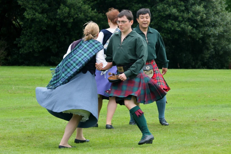 people walk through the grass in their kilt clothing