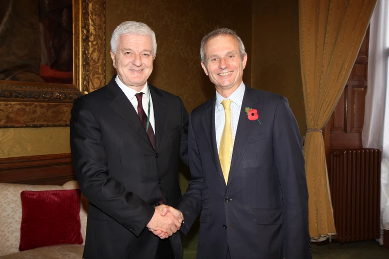 two men shaking hands in a room with gold curtains