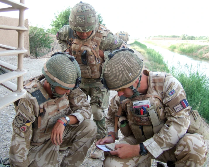 a group of soldiers look down at a cell phone