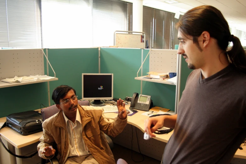 an office setting with two people, one is holding a device in his hands and another holding a wii remote