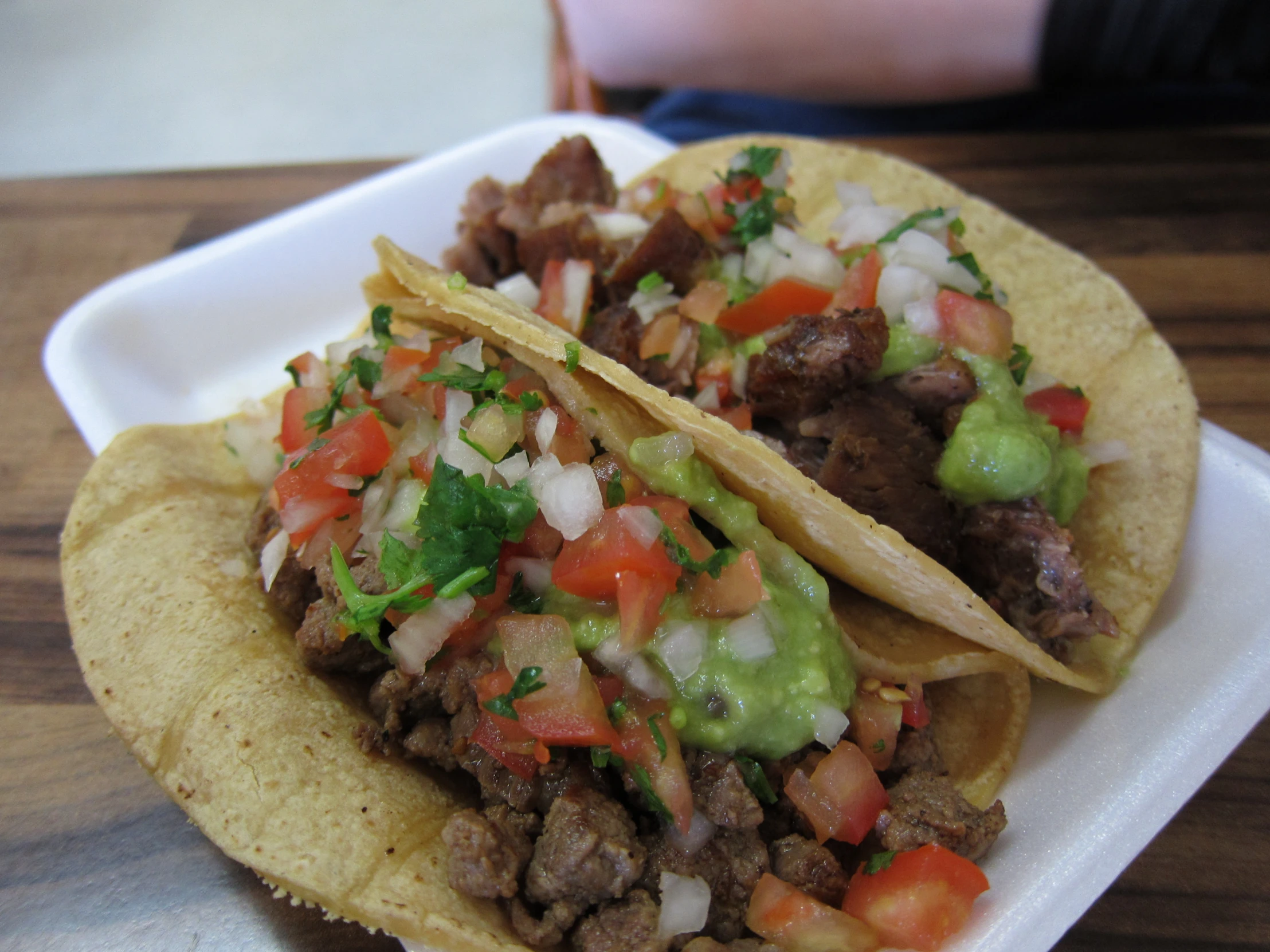 two tacos sitting on a plate with onions, meat, and cheese