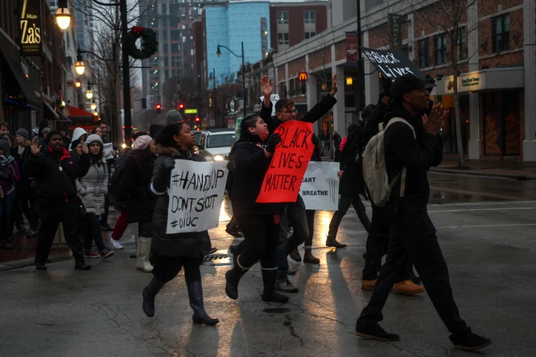 a group of protesters march down a street holding up signs