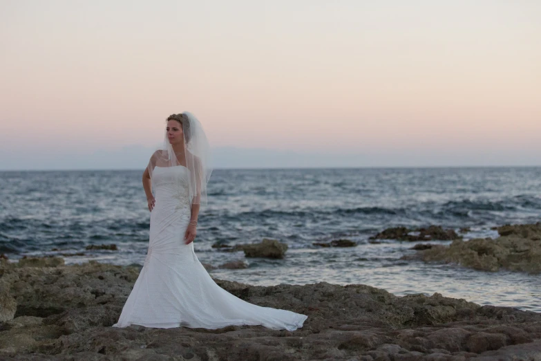 a beautiful young bride posing for the camera in front of the ocean