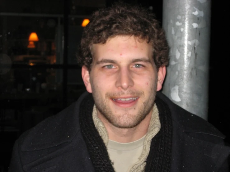 a man with curly hair wearing a dark jacket and scarf