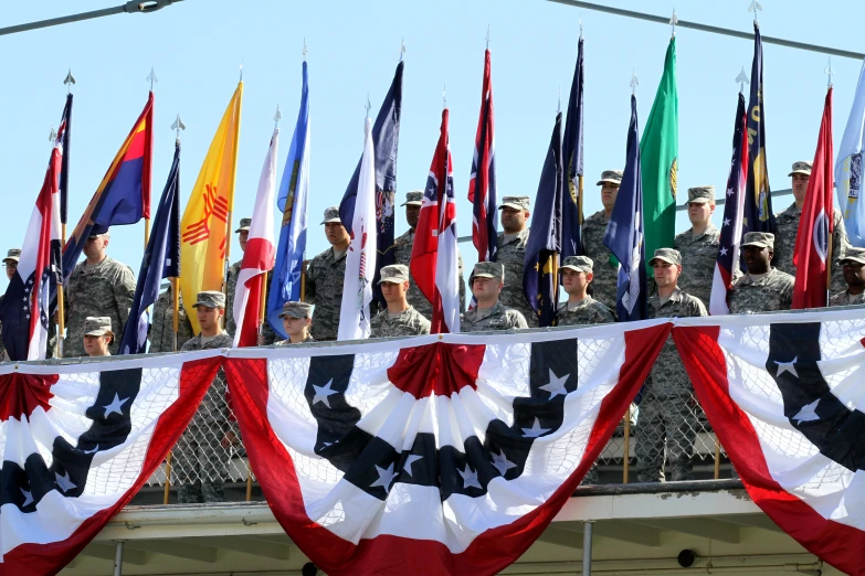 a row of flags flying in the sky above two rows of men and women