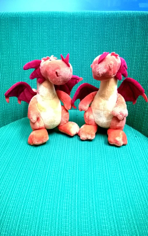 two stuffed dragon figurines sitting on top of a green couch