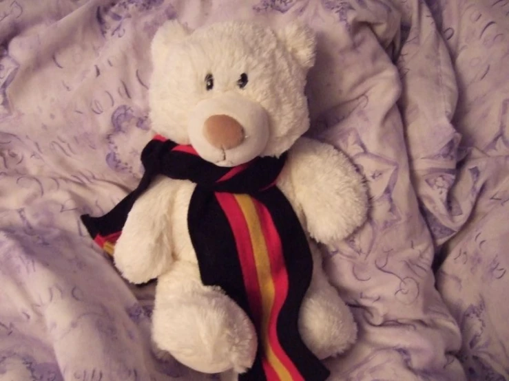 the teddy bear is wearing a scarf on the bed