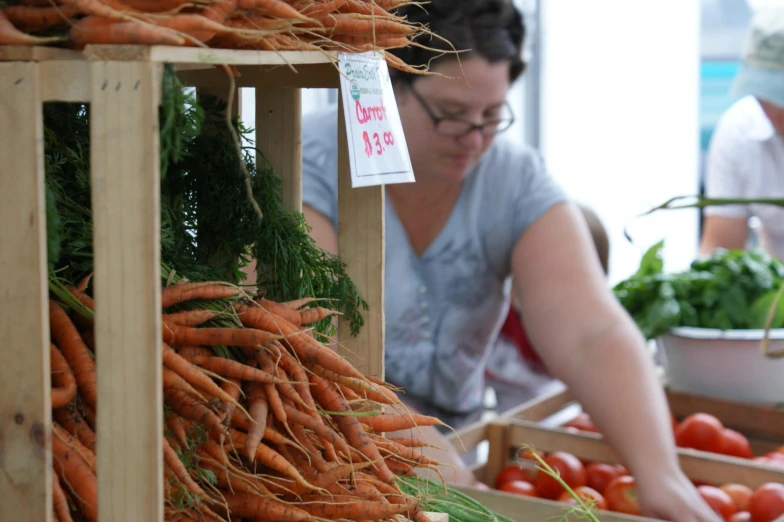 a woman standing next to a pile of carrots