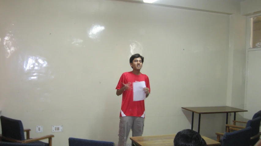 man in red shirt with arms crossed in front of a group of chairs