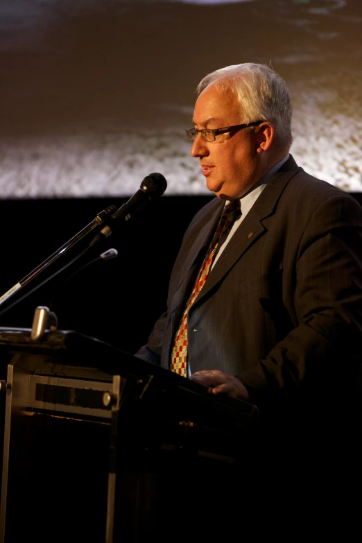 a man with glasses speaking at a podium