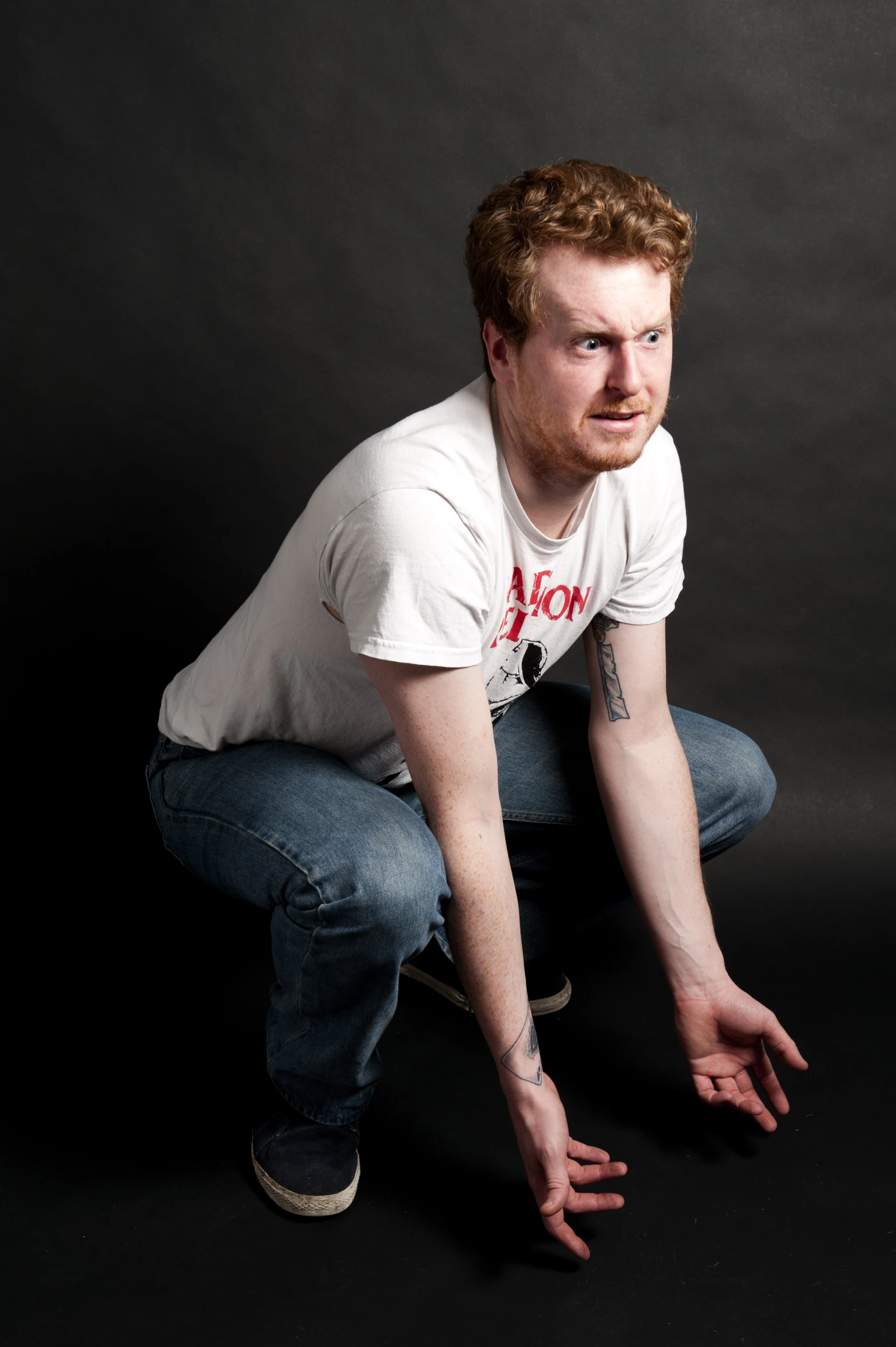 a red headed man squatting in front of a gray background