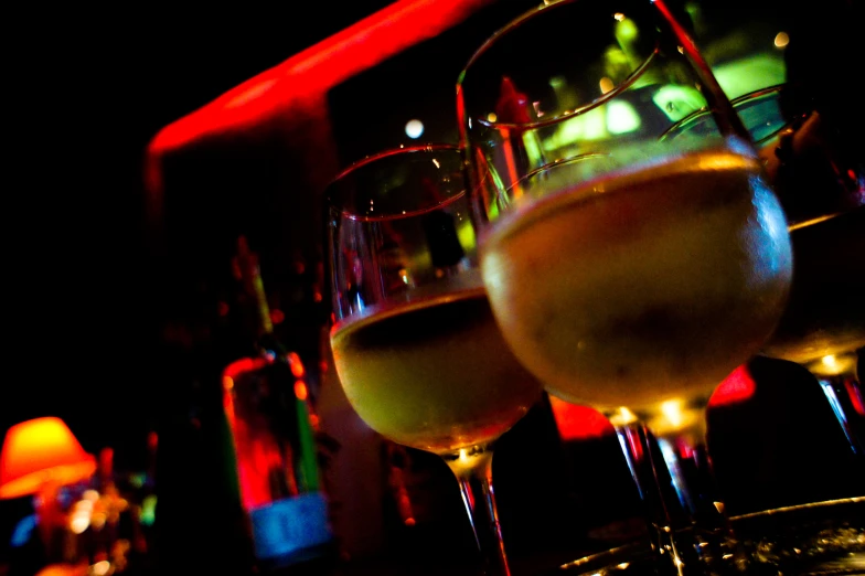 three glasses of wine sit on a bar, with red and green lighting behind them