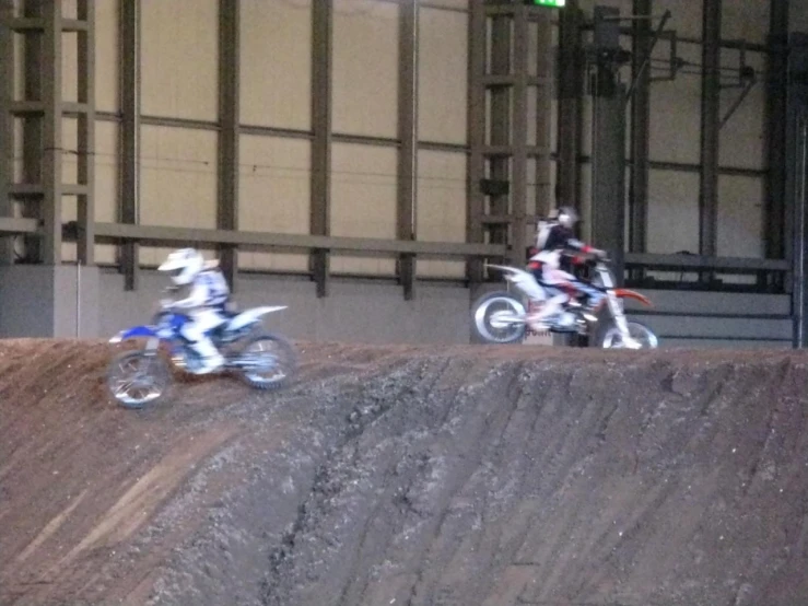 two motorcycles on dirt course in large indoor facility