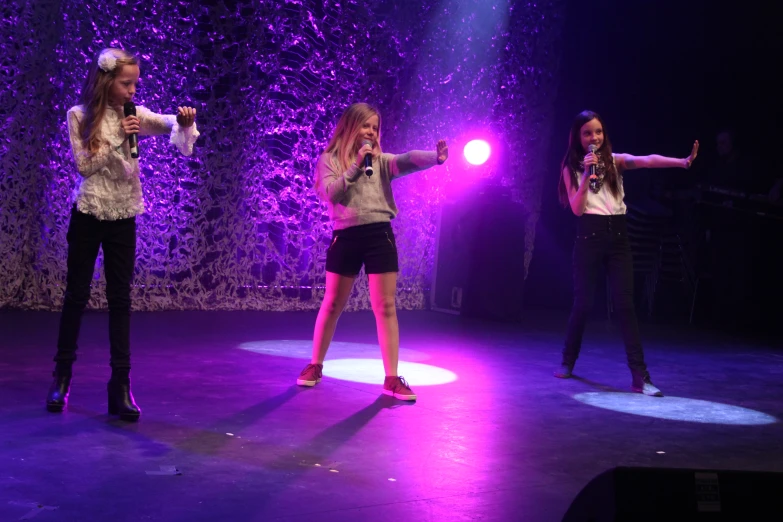 three young women singing on stage with one holding a light