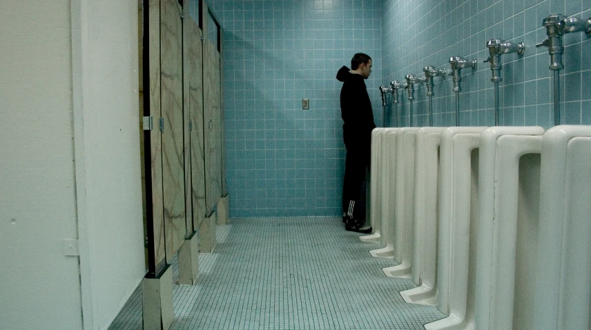 a bathroom with a row of urinals and a woman standing at the front