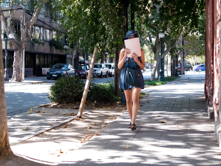 a woman holding up a piece of paper walking down the sidewalk