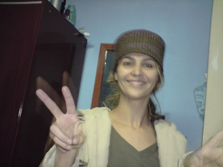 a woman standing in a room holding up a peace sign