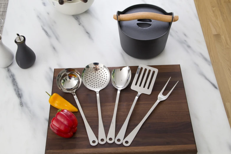 utensils sit on a  board, next to a cup and pepper shaker