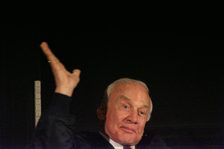 a close up of an older man in a suit and tie pointing upward