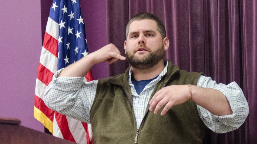 man standing at podium with large american flag