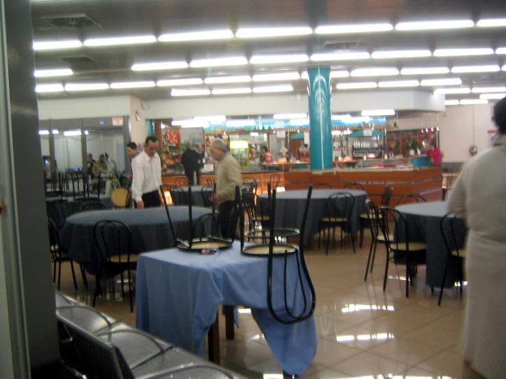 there are many tables and chairs with blue linens on it