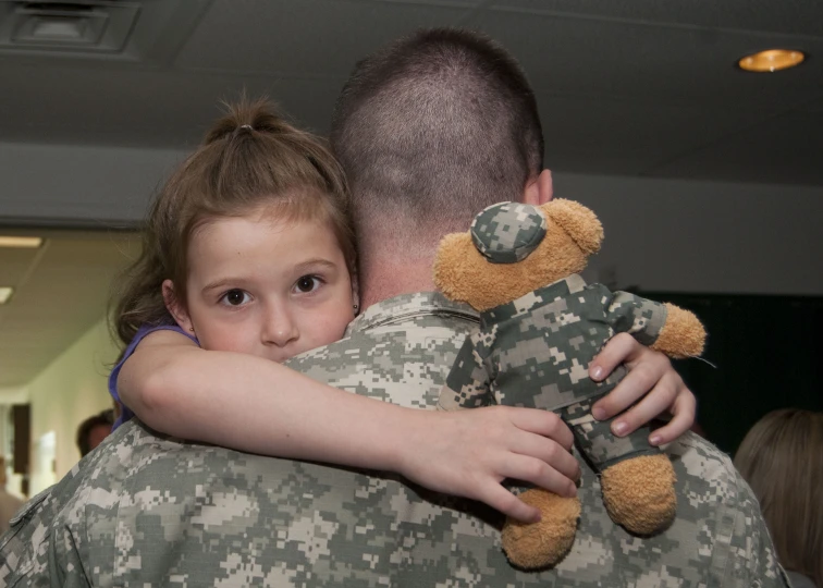 soldier hugging child in uniform holding up teddy bear