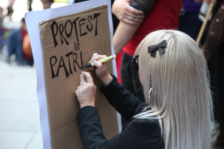 a woman writes on a protest sign with black lettering