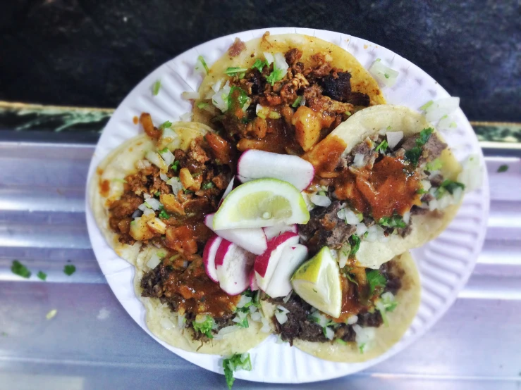 tacos with meat, onions, limes, onions and sauce on a paper plate