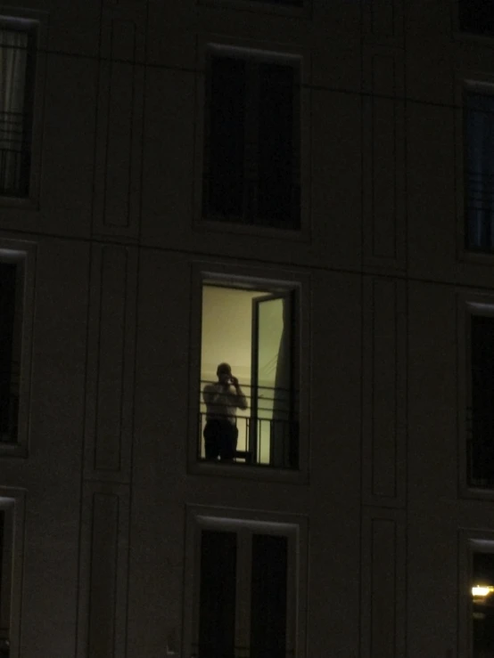 a person standing in a window next to a building at night