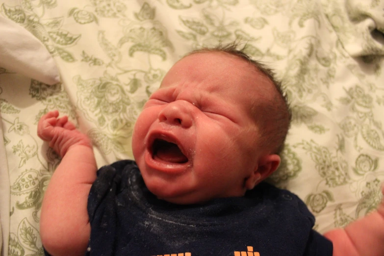 a baby boy is yawning while laying on his stomach