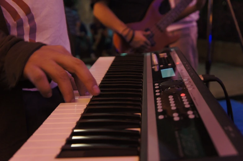 an individual plays the electronic keyboard while another sits next to him