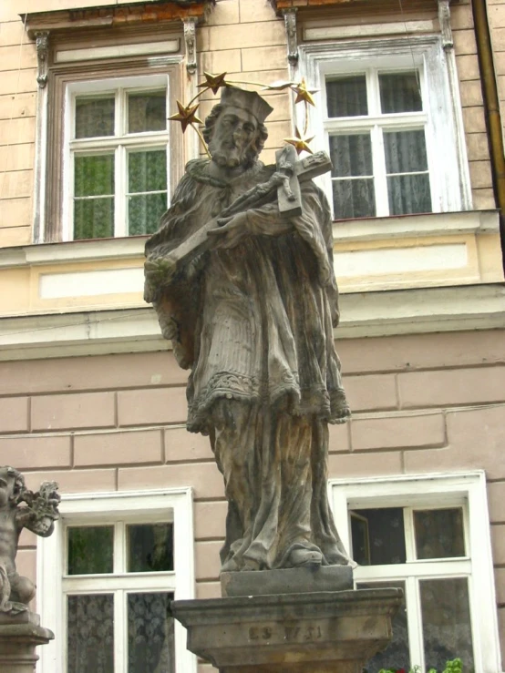 a statue with a cross in his hands standing in front of an apartment building