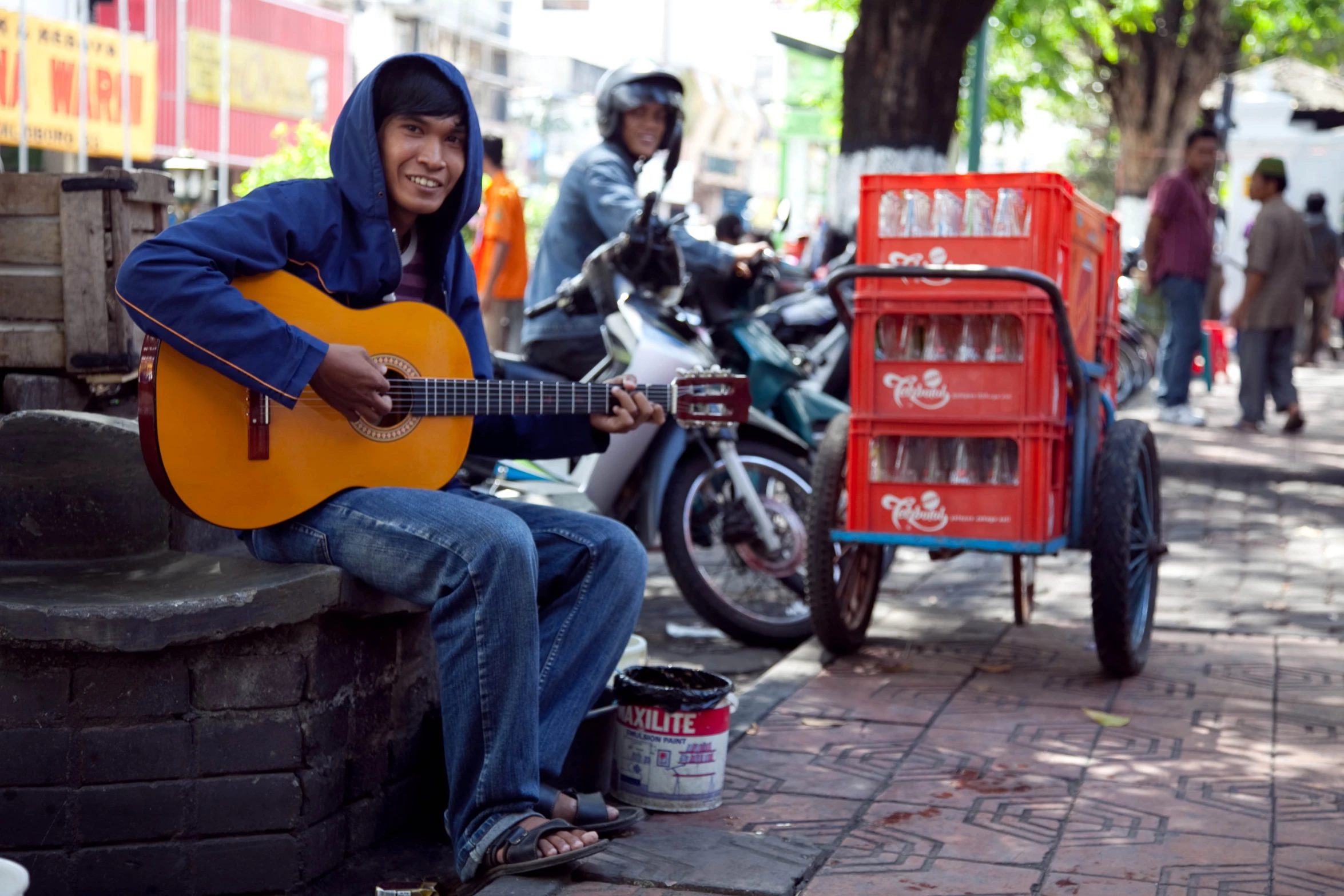 an indian man sits on the curb playing a guitar