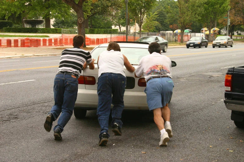 three people hing a car in the road