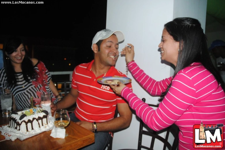 two people eating cake with one woman standing next to them