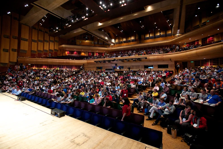 many people are sitting in an auditorium as they watch a speaker