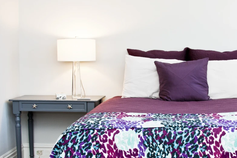 an elaborate purple and white bed sits near a nightstand