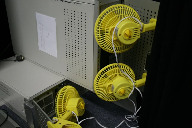 some yellow fans on a wall near two power cords